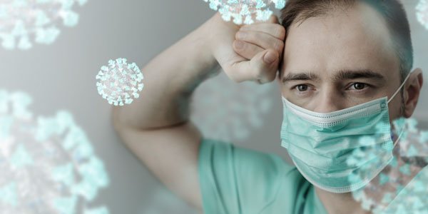 Hombre descansa arrecostado a una pared con tapabocas